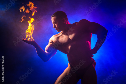 A man with an inflated torso. Handsome bodybuilder with fire in hands. Bodybuilder on a blue background.