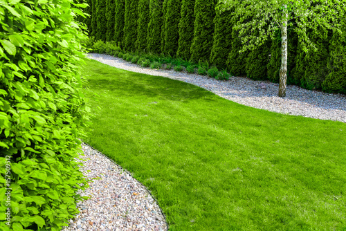 Well maintained formal garden with a path of small stones, hedgerow and green lawn - focus on background