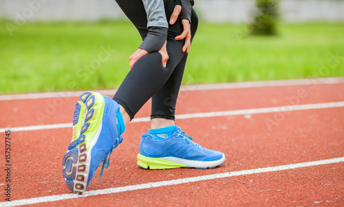 Athletic woman on running track has calf cramp and touching hurt leg