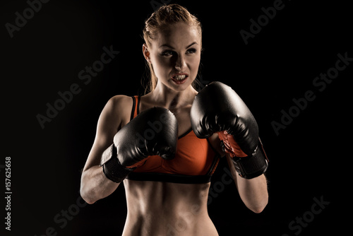 Close-up view of aggressive young sportswoman boxing in boxing gloves isolated on black