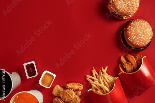 Two hamburgers and french fries, sauces and drinks on red background. Fast food. Top view, flat lay with copyspace