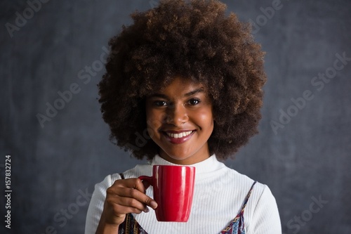 Smiling woman with frizzy hair holding coffee mug against wall