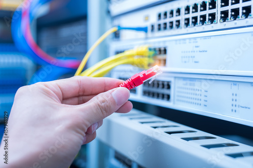 man working in network server room with fiber optic hub for digital communications and internet