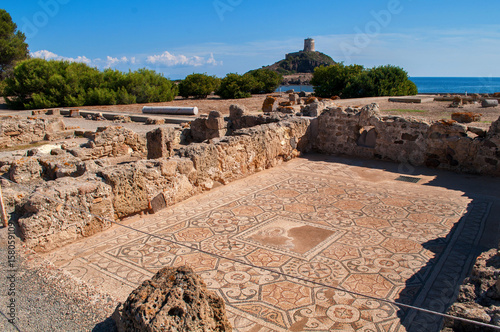 Excavations in Nora, Sardinia, Italy. Mosaic floor and behind it an old watchtower on a hill above the sea.