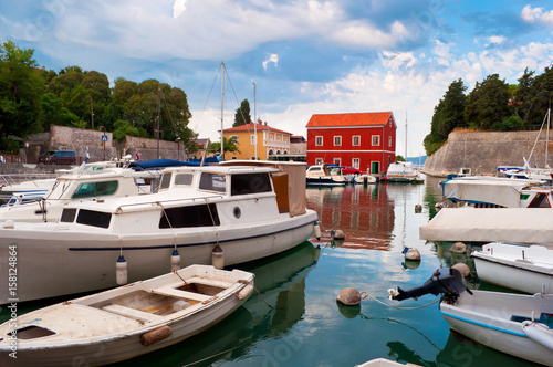 Cozy picturesque town of Zadar, Croatia. Red and orange houses among green trees near the water where numerous boats and yachts are floating. Dramatic cloudy morning sky