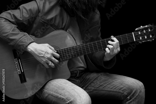 Long hair male guitarist playing with acoustic guitar in leather jacket on the stage.