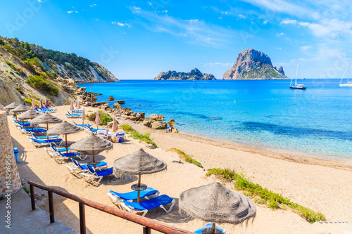 View of Cala d'Hort beach with sunbeds and umbrellas and beautiful azure blue sea water, Ibiza island, Spain