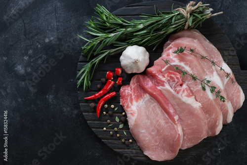 Wooden chopping board with raw seasoned pork meat steaks. Dark metal background, flat-lay, copyspace