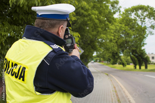 Kontrola radarowa przy drodze wojewódzkiej. Policjant dokonuje pomiaru prędkości w terenie zabudowanym.