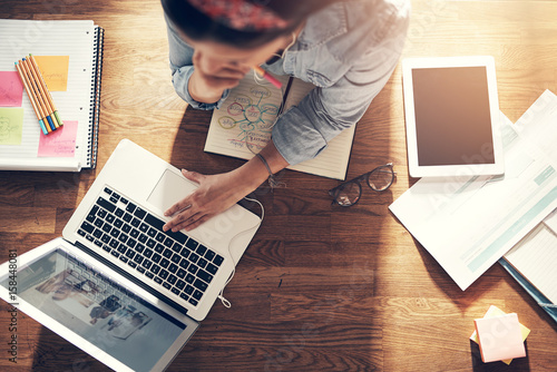 Young female entrepreneur thinking and browsing laptop in office