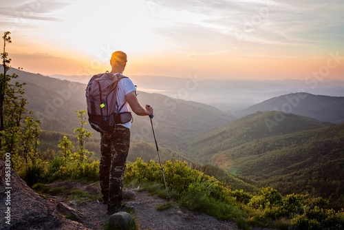 Man tourist with trekking poles on top of hill at sunrise