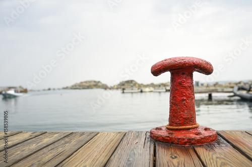 Red bollard with a mooring rope on the pier at the port and sea water in the background. Sardinia, Italy..