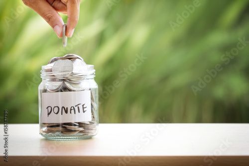 Hand putting Coins in glass jar for giving and donation concept