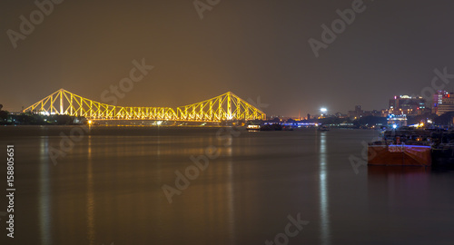 Historic Howrah bridge and Kolkata cityscape as seen from Princep Ghat in night illumination.