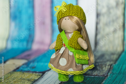Текстильная куколка со светлыми волосами, в платье в горошек, в зеленых вязанных шапочке и жилете, в кедах из зеленого фетра и с сумочкой их фетра