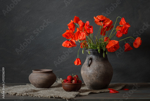 Still life in a rustic style: potteries, strawberry and a bouquet of red poppies