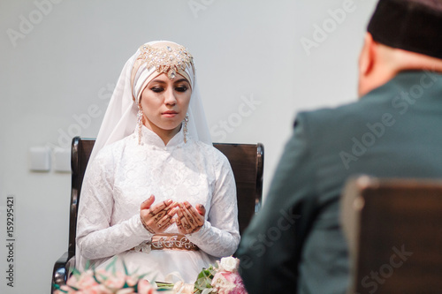 Islamic woman in wedding dress praying in mosque with mullah