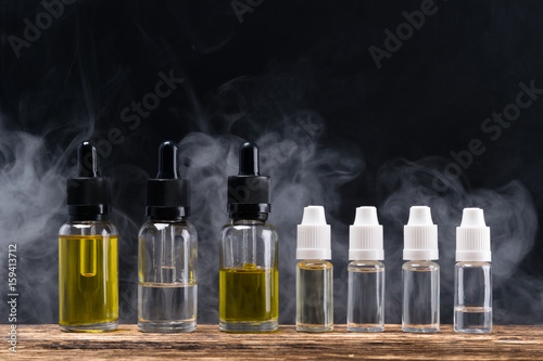 Liquid with tasty aromas in bottles for an electronic cigarette, against a background of steam