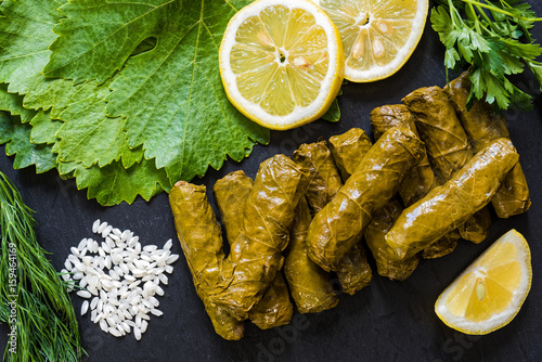 Delicious stuffed grape leaves (the traditional dolma of the mediterranean cuisine) on black dish with leaves, lemon slices, rice, parsley and dill