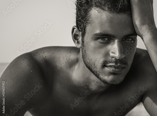 Sexy closeup portrait of handsome topless male model with beautiful eyes on the beach. Black and White.