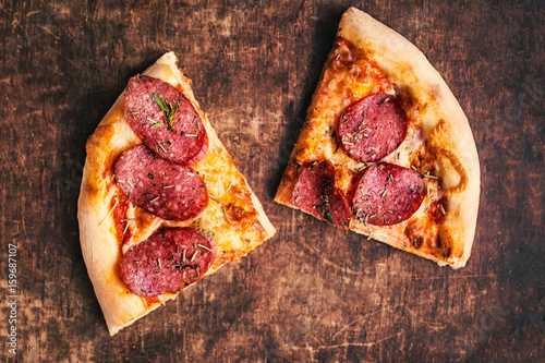 Slice of fresh italian classic original pizza with cheese mozzarella, pepperoni and salami on a rustic wooden table.
