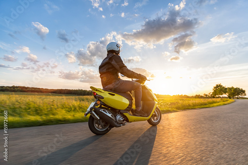 Motorbiker riding on empty road with sunset sky