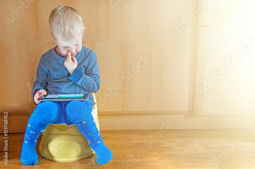 little boy on potty with tablet pc on the white carpet.