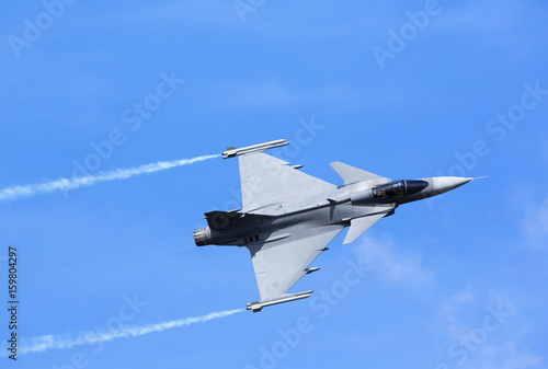 Modern jet fighter flying against a blue sky. White smoke trail.