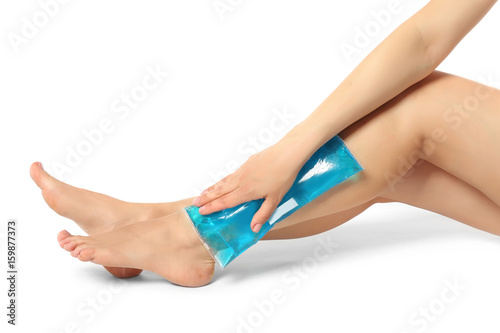 Young woman applying cold compress to leg on white background. Legs pain concept