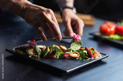 Chef sprinkling spices on dish in commercial kitchen