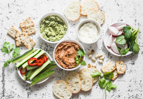 Vegetarian dip table. Eggplant, harissa, walnuts dip, broccoli dip, soft tofu and fresh vegetables on a light background, top view. Flat lay
