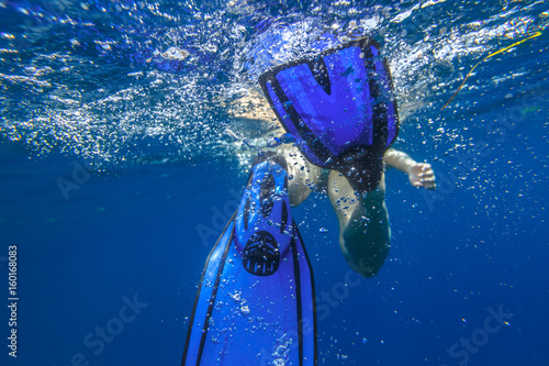 Closeup of blue fins of underwater female apnea while swimming. Bubbles of water. View from behind snorkeler woman in underwater activity. Watersport and leisure concept. Fins slamming into sea.