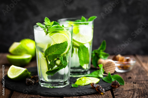 Refreshing mint cocktail mojito with rum and lime, cold drink or beverage with ice on black background