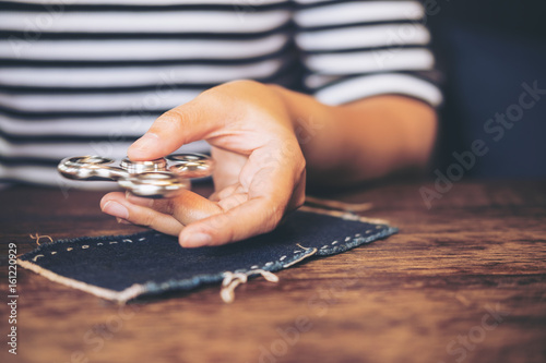 A woman's hand holding and playing fidget spinner on vintage wooden table