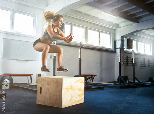 Fitness woman jumping on box training at the gym, crossfit exercise