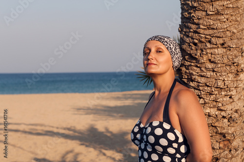 Middle aged woman at the beach. Portrait of tanned beautiful female in her 40 50 years old wearing swimsuit and enjoying summer vacation holiday trip. Sea and sand background.