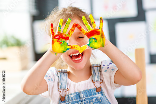 funny child girl draws laughing shows hands dirty with paint