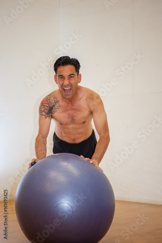 Middle age Japanese man performing push up on stability ball with intense expression and strong core.