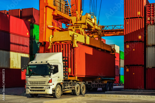 Container truck or Rubber Tired Gantry Cranes (RTG) picking up a container at yard. Port logistics, container yard operation. 