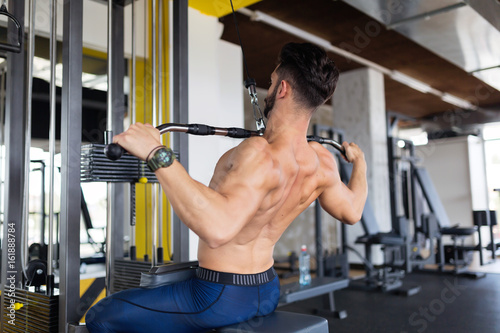 Handsome young man working on lat machine