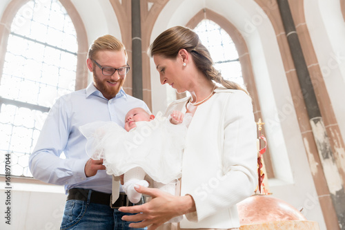 Junge Eltern mit ihrem Baby im Taufkleid in einer Kirche