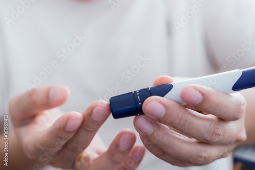Medicine, diabetes, glycemia, health care and people concept - close up of man hands use lancet on finger to checking blood sugar level by Glucose meter
