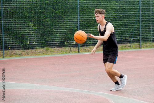 Teenage boy bouncing a basketball on a court