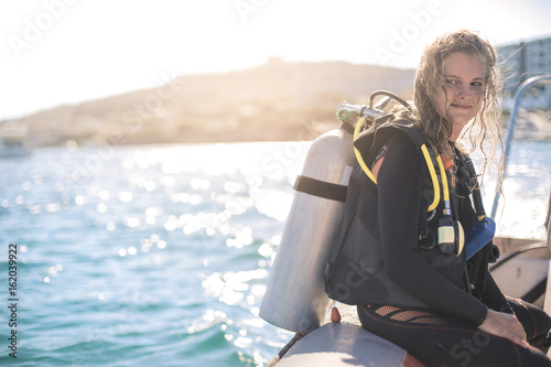Beautiful girl wearing scuba diver's equipment, sitting on a boat