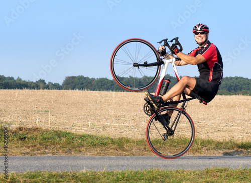 Cheerful cyclist riding on the rear wheel. Biker balancing while driving on a road bike. Risky ride on one wheel.