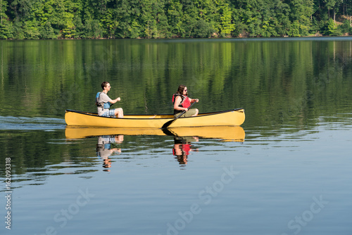 Couple paddling in yellow canoe on tree lined lake