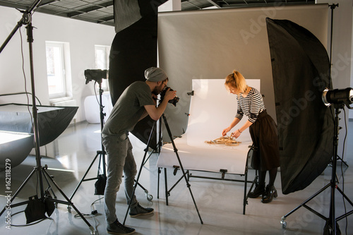 Creative team shooting commercials. Back view of photographer taking object shots with assistant in studio interior. photoshoot backstage