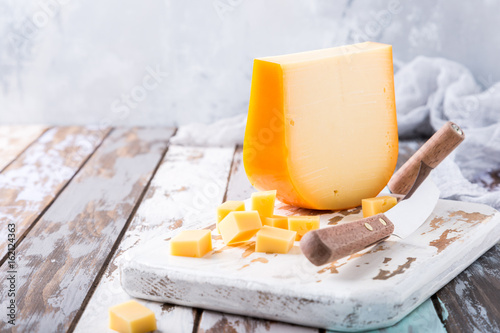 Delicious dutch gouda cheese with cheese cubes and special knife on old wooden table. Copy space.