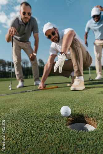 young professional golf players looking at ball near the hole