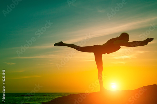 Yoga and healthy lifestyle. Silhouette of fitness woman doing exercises on the sea beach during amazing sunset.
